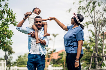 Wall Mural - Portrait of enjoy happy love black family african american father and mother with little african girl child smiling and play having fun moments good time in park at home