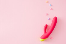 Sexual Pleasure Toy Subject. Top View Flat Lay Of Dual Vibrator, Colorful Hearts On Pastel Pink Background With Empty Space For Message Or Advert
