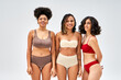 © LIGHTFIELD STUDIOS - Smiling multiethnic women in colorful lingerie looking at camera together and standing isolated on grey, different body types and self-acceptance, multicultural representation, cultural diversity