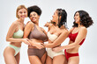 © LIGHTFIELD STUDIOS - Positive multiethnic women in colorful bras and panties hugging while posing and standing together isolated on grey, different body types and self-acceptance concept, multicultural representation