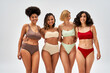 © LIGHTFIELD STUDIOS - Cheerful and sexy multiethnic women in colorful lingerie hugging and looking at camera together isolated on grey, different body types and self-acceptance, multicultural representation