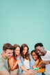 © Jose Calsina - Vertical portrait of multiracial group of young friends smiling using their mobile phone app at teal blue wall background. Diverse teenage student people having fun watching content on a social media