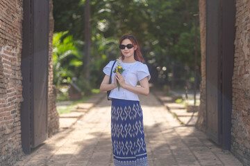 Wall Mural - Pretty Asian tourists woman wearing beautiful hand-woven clothes dyed with indigo and mud-fermented natural colors modern Thai traditional dress costumes are popular in ancient temple Thailand.