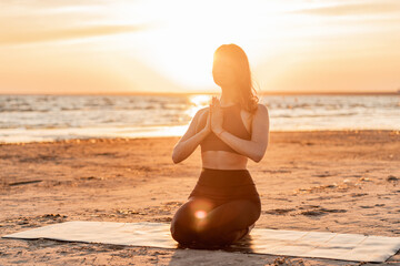 The trainer uses an aerobics mat at sunset. Balance and meditation woman training yoga asana outdoors near the lake. Peace and harmony.