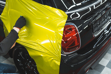 unrecognizable car wrapper in black protective gloves using squeegee to straighten neon yellow vinyl