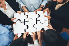 Diverse Corporate Officer Workers Collaborate In Office, Connecting Puzzle Pieces To Represent Partnership And Teamwork. Unity And Synergy In Business Concept By Merging Jigsaw Puzzle. Concord