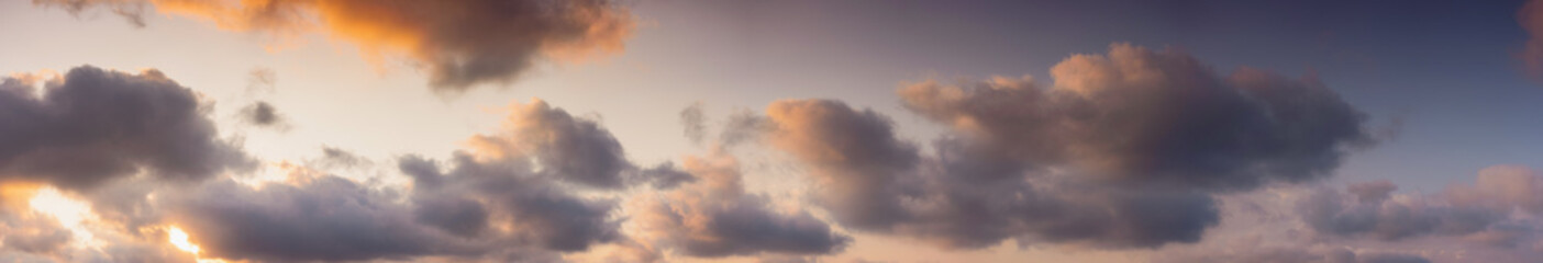 Wall Mural - panorama of a sky in warm evening light. massive clouds in orange color at sunset