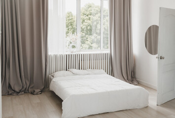 Interior of a white bedroom with curtains and white pillows on a wooden bed, a classic for relaxing and sleeping. The modern white bedroom is bright.