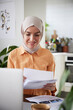 © Johnér - Smiling woman with hijab checking bills at home