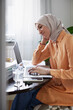 © Johnér - Smiling woman with hijab working from home using laptop