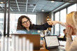 © Johnér - Smiling woman giving fist bump to colleagues in office