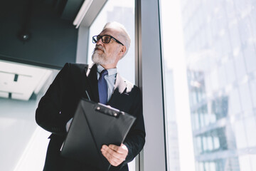 Sticker - Senior businessman with clipboard standing near glass wall