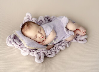 Wall Mural - Newborn baby girl sleeping on knitted pillow and blanket. Cute infant child kid napping and holding hands under cheek in studio