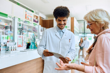 Poster - Happy Middle Eastern pharmacist using touchpad while assisting senior woman in pharmacy.