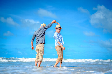 Wall Mural - Plan life insurance of happy retirement concepts. Senior couple dancing at the beach looking the ocean on a good day in sunny day morning.