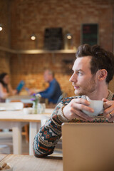 Wall Mural - Pensive man looking away drinking coffee at laptop in cafe