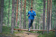 Runner Jumping Over Fallen Tree On Trail In Woods