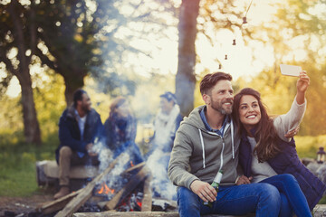 Wall Mural - Smiling couple taking selfie with camera phone near campfire