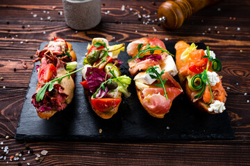 Wall Mural - Appetizers bruschettas with beef slices, capers, cherry tomatoes, mozzarella, salmon, cucumber, lettuce.