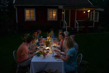 Family enjoying candlelight dinner at patio table outside house at night