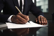 Businessman in a suit signs a contract with a pen while sitting at a table in the office.
