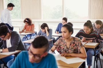 Wall Mural - Professor watching college students taking test at desks in classroom