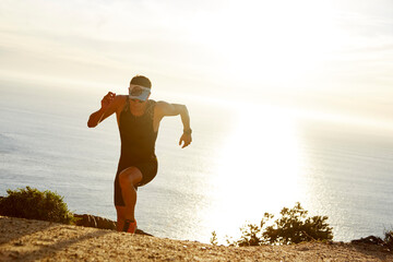 Wall Mural - Male triathlete runner running uphill on sunny ocean trail