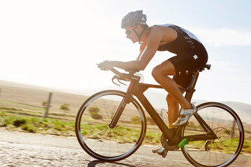 Male triathlete cyclist cycling on sunny rural road at sunrise