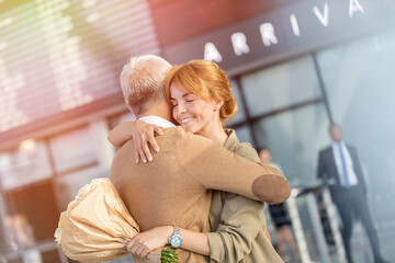 Wall Mural - Husband and wife with flowers greeting and hugging in airport