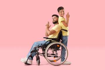 Wall Mural - Little boy and his father in wheelchair showing gun gesture on pink background