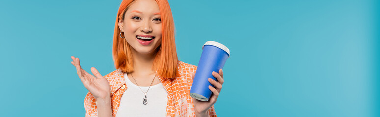 positivity, coffee to go, happy asian and young woman with red hair holding paper cup and looking at camera on blue background, casual attire, generation z, coffee culture, hot drink, amazed, banner