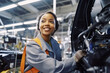 © MariaEugenia - Smiling black woman working in car factory. Created with AI.