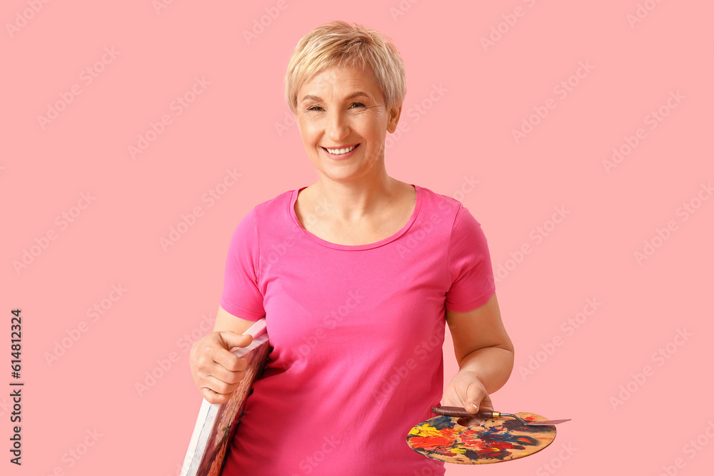 Mature female artist with tools and picture on pink background