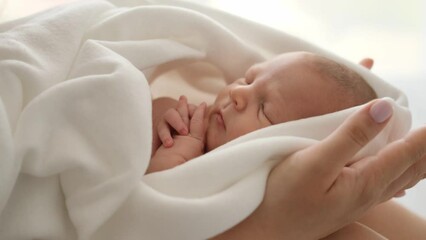 adorable newborn baby sleeping on his mother hands. closeup view of infant child swaddled in blanket
