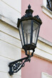 A black lantern with a lot of beautiful elements, located on the facade of a building painted in white and pink