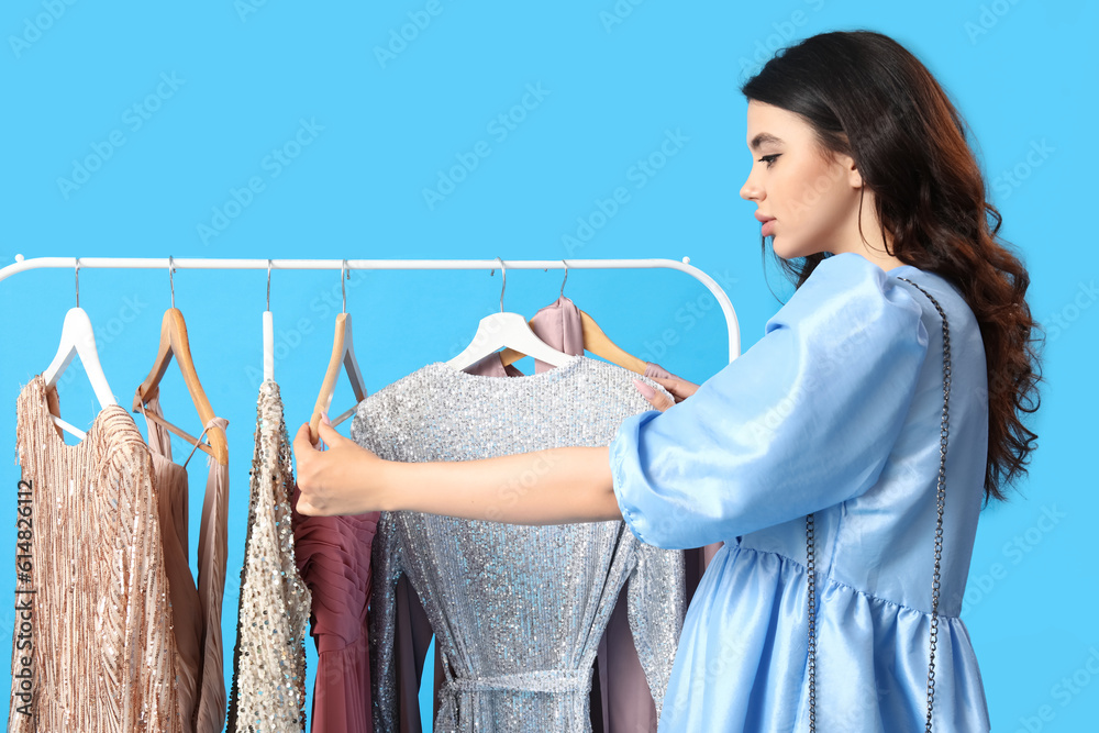 Young woman choosing prom dress on blue background
