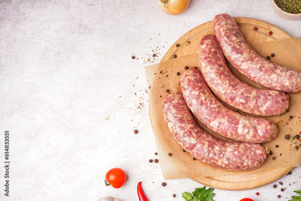 Wooden board with raw homemade sausages on light background