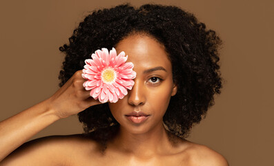 Wall Mural - Beautiful young black woman holding flower over her eye