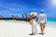A tourist couple walks down a beautiful beach in Krabi, Thailand with fine sand a longtail boats during their summer vacations