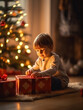 © Валерия Бельчикова - A boy in a white sweater sits at home by the Christmas tree and unpacks his gift with a smile. Christmas card. New Year's gift under the tree. New year and merry christmas concept.