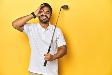 Wall Mural - Young Latino golfer with club and cap on a yellow studio background, excited keeping ok gesture on eye.