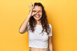 Young Caucasian woman, yellow studio background, excited keeping ok gesture on eye.