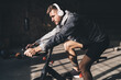 © BullRun - Muscular man in headphones riding exercise bicycle in gym