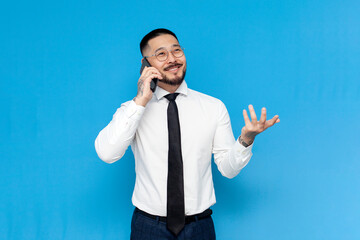 Wall Mural - successful asian businessman in white shirt and tie talking on the phone on blue isolated background