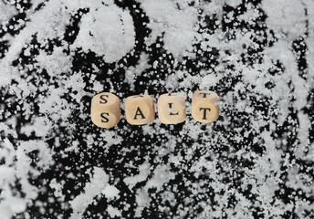 Wall Mural - Salt alphabet letter word bead fly with crystal sodium. Less Salty concept to reduce seasoning food. Salt letter word on health care concept. Black background isolated