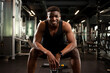 young athletic african american man sits in dark gym and smiles, athletic guy rests in fitness club