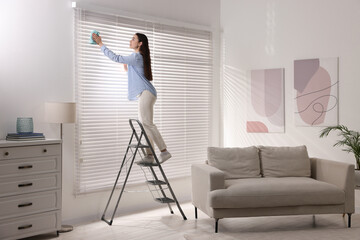 Sticker - Woman on metal ladder wiping blinds at home