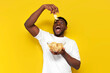 joyful african american man holding plate of chips and biting snack on yellow isolated background