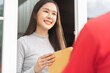 Delivery service asian young customer woman hand received cardboard box parcel from messenger male. Postman in red uniform holding cardboard box parcel, carton send to client at home, shopping online.