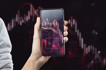 Wall Mural - Online trading, bearish market and economy recession concept with digital financial chart falling candlestick and graphs on smartphone screen in human hand on dark stock market background